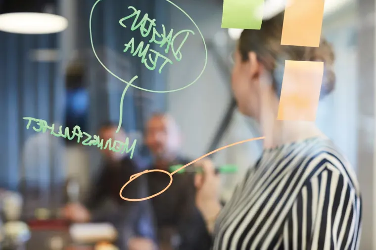 F&auml;rgade post-it-lappar med handskriven text f&auml;sta p&aring; en glasv&auml;gg, med aff&auml;rskl&auml;dda personer i bakgrunden.