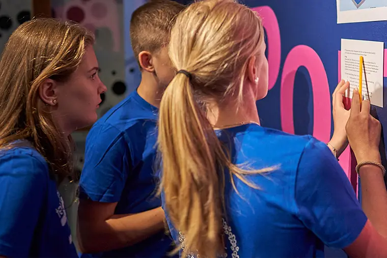 Tre ungdomar läser på ett papper med text.