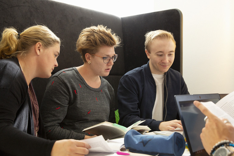 Studenter sitter i grå soffa med böcker och dator.