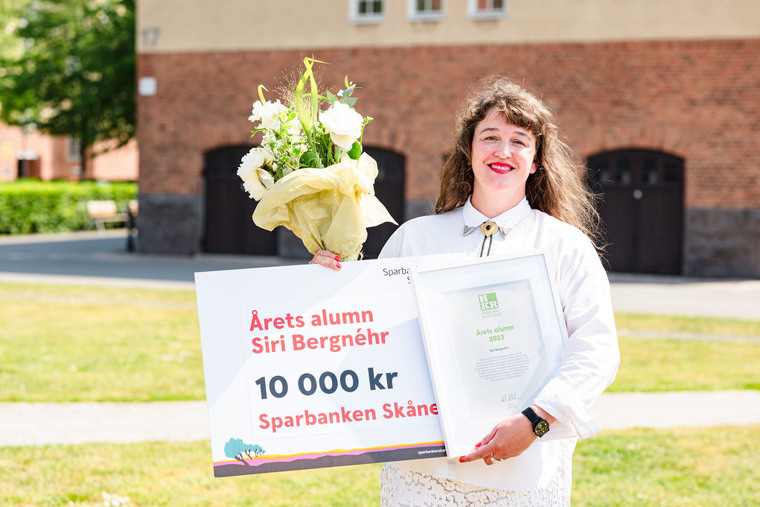 Siri visar stolt upp diplom och blommor, leendes mot kameran