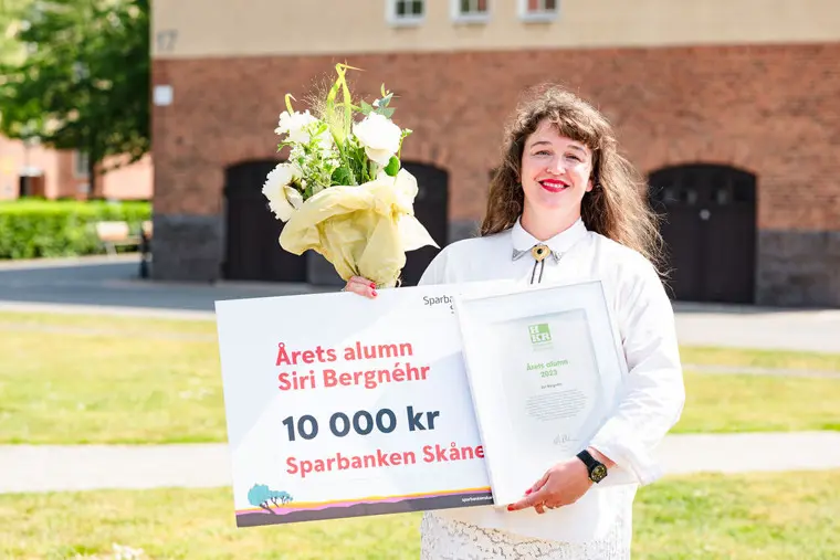 Siri visar stolt upp diplom och blommor, leendes mot kameran