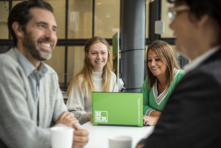 Four people around a table, with laptop and cooffee mugs.