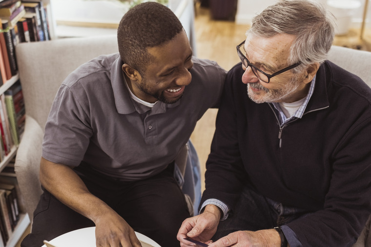 Happy male caregiver teaching online shopping to senior man on laptop at nursing home