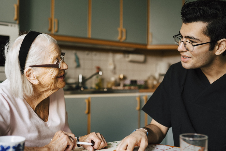Smiling senior woman talking with male nurse in kitchen at home