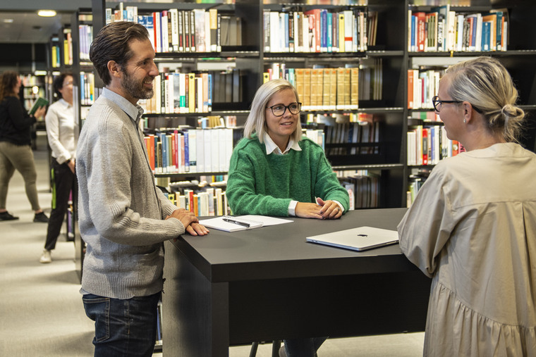 Tre personer samtalar runt ett bord i biblioteket.