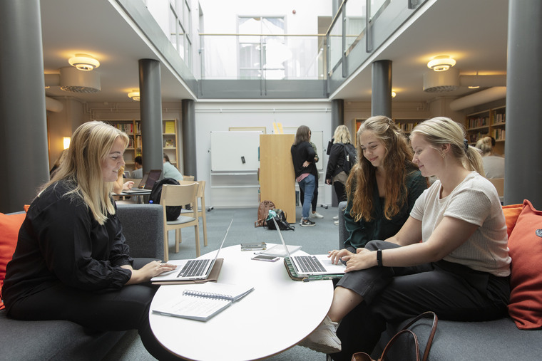 Tre tjejer sitter i grå soffa i biblioteket.