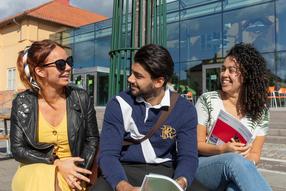 Tre studenter sitter utomhus på en bänk.