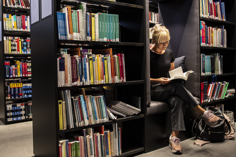 Kvinnlig student sitter och läser en bok i biblioteket.