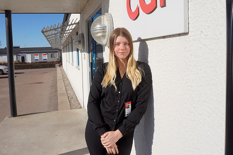 Lizette står i solen utanför sin arbetsplats och tittar in i kameran
