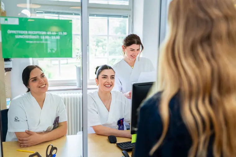 Tre studenter står i receptionen och hjälper besökare.