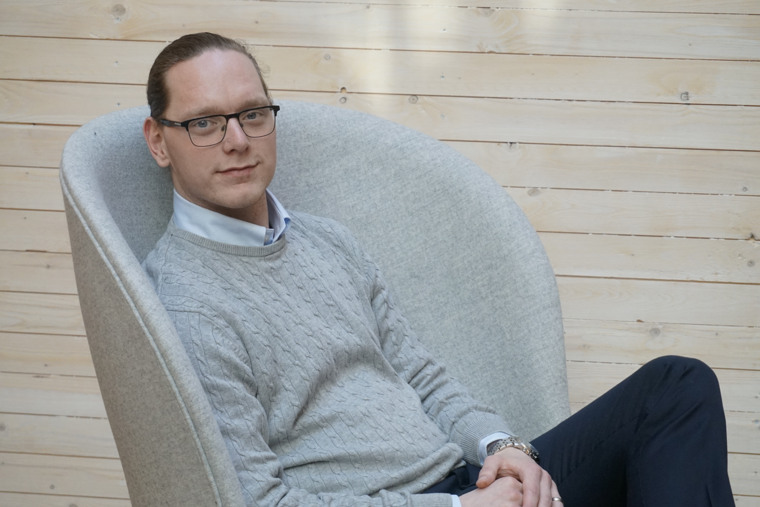 Robin Lund sitter i en grå fåtölj och ler in i kameran