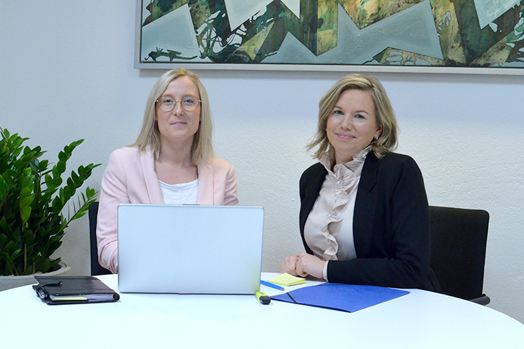 Anna och Maria sitter tillsammans vid ett bord och tittar in i kameran.