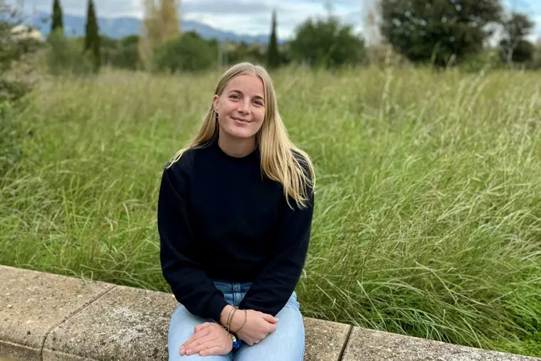 Simone sittandes p&aring; en stenmur med h&ouml;gt gr&auml;s i bakgrunden