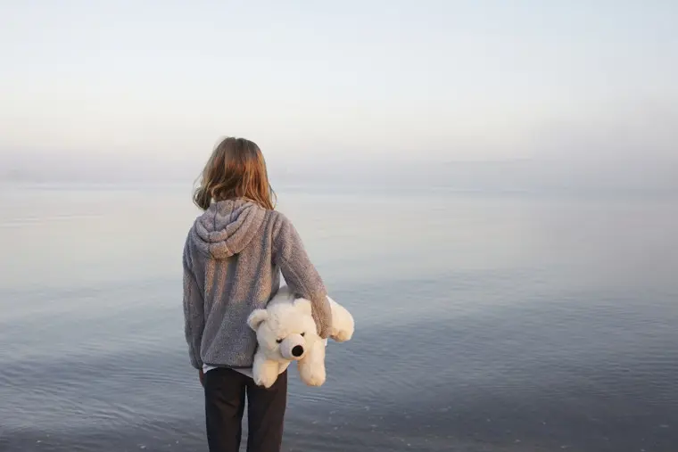 Ett barn h&aring;ller i en nalle och blickar ut &ouml;ver havet. 