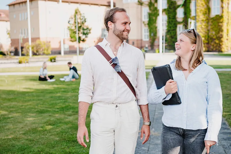 Två studenter samtalar utomhus på högskolans campus.