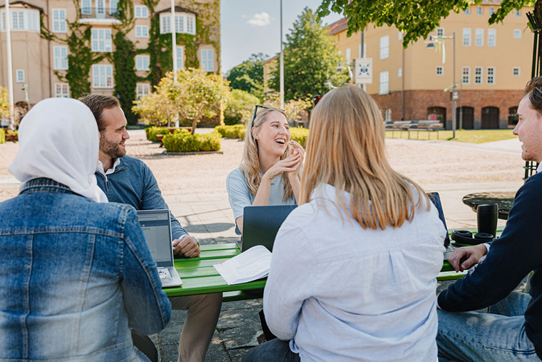 Studenter sitter utomhus runt ett bord.