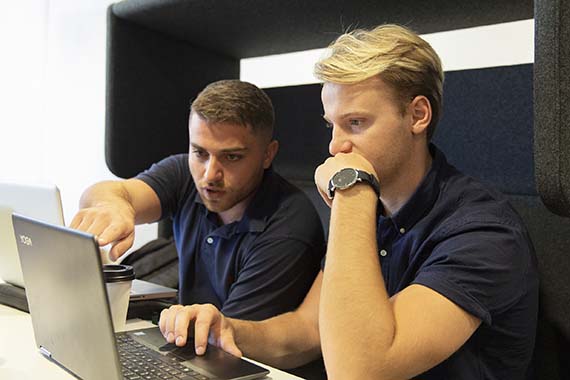 Två studenter sitter i en soffgrupp och tittar på en datorskärm